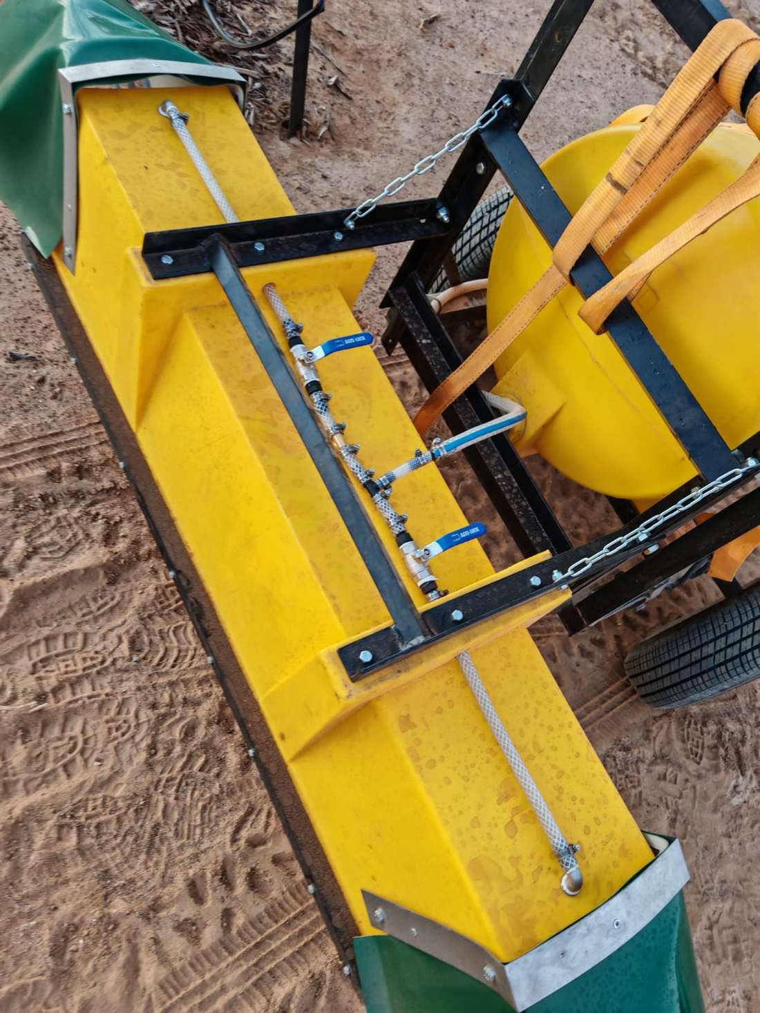 Yellow trough spreader with feeder chains parked on prepared ground before a slug-pellet run.