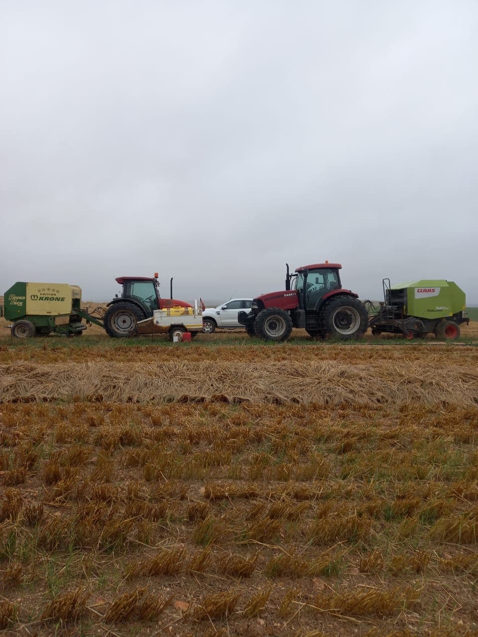 Two tractors with two round balers and a bakkie staged at the edge of a stubble field before the day's run.